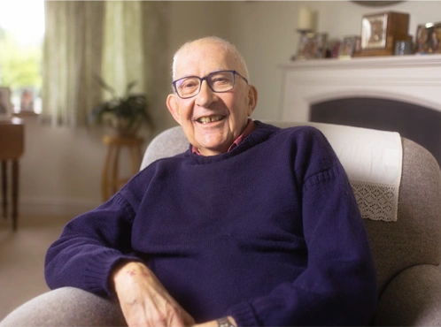 smiling Man on arm chair in purple sweater